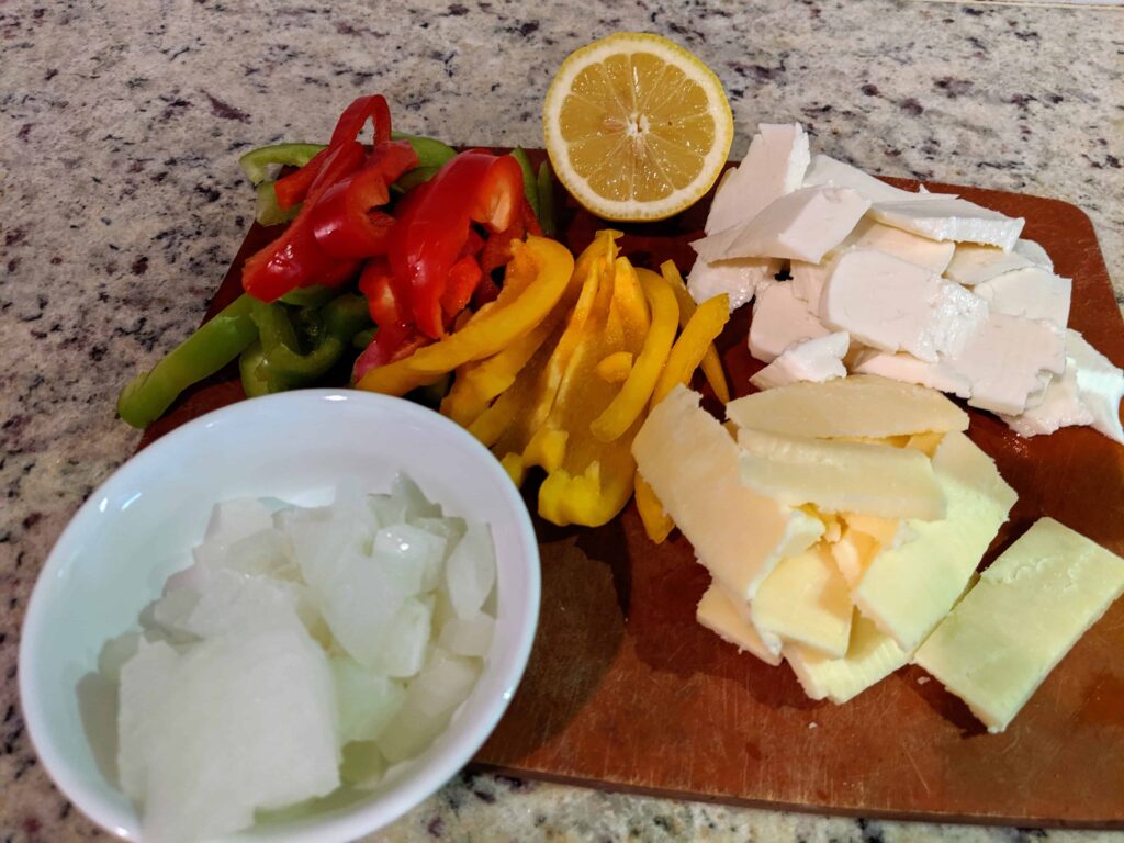 different cheeses, bell pepper, lemon, onion on a cutting board.
