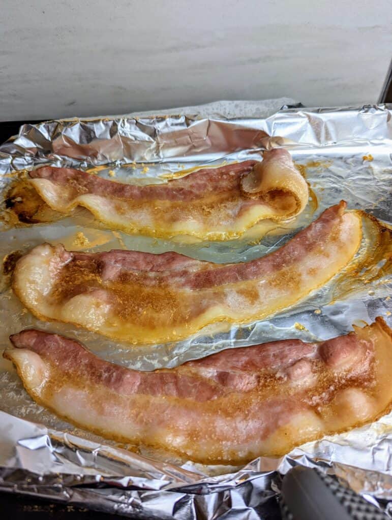 bacon cooked half-way on a baking sheet with foil