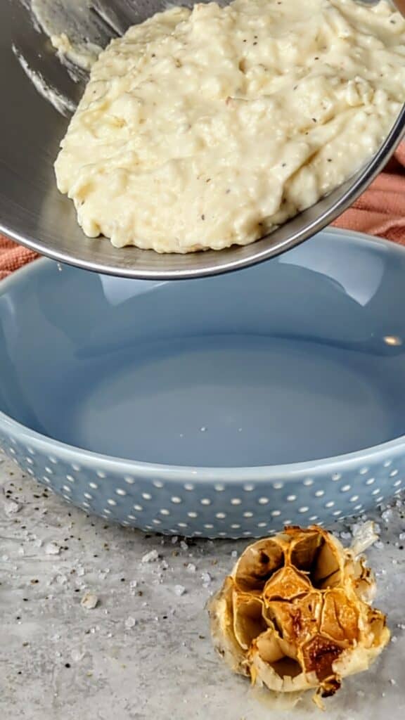cooked roasted garlic mashed potatoes pouring into a bowl
