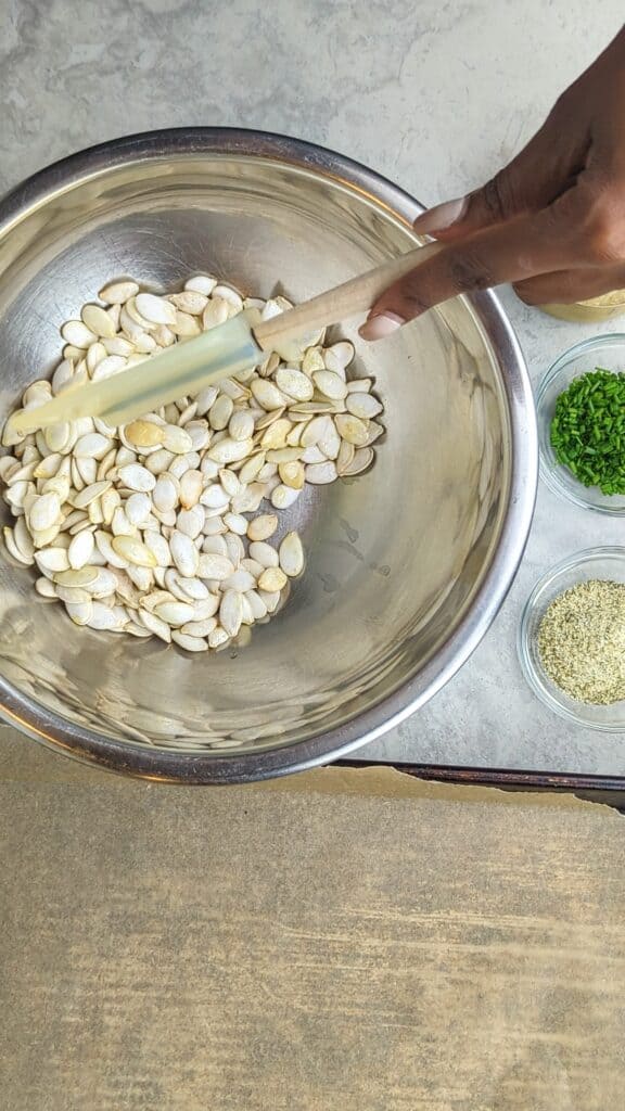 mixing ranch pumpkin seeds in a silver bowl with a rubber spatula
